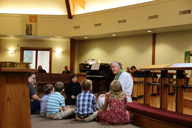 Pastor sits in front on the floor talking to group of children